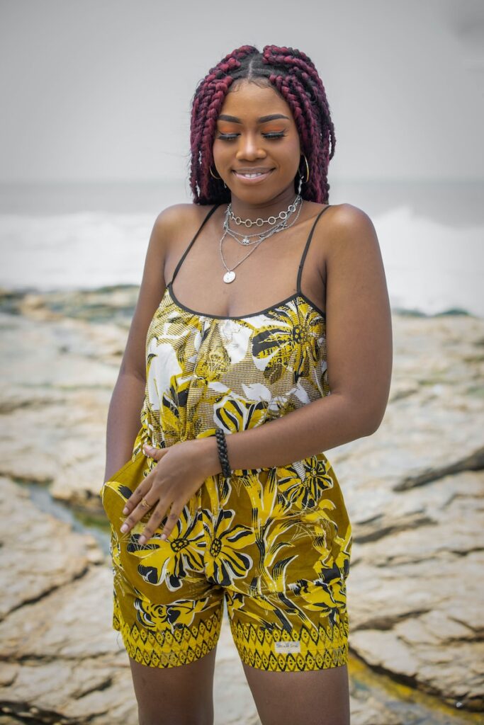 a woman in a yellow and black dress standing on a rocky beach